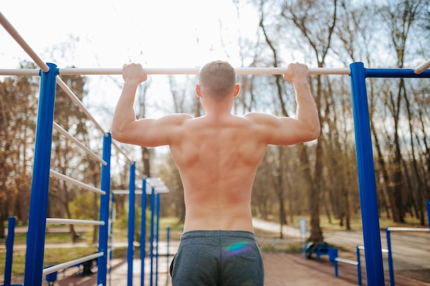 Ein Outdoor-Workout-Mann führt intensive Ziehungen an einer Bar durch. Ein fitter Mann trainiert seinen Oberkörper, indem er nake macht.