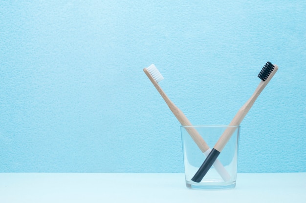 Ein paar bambuszahnbürsten in einem transparenten glas auf einem blauen hintergrund mit einem kopienraum.