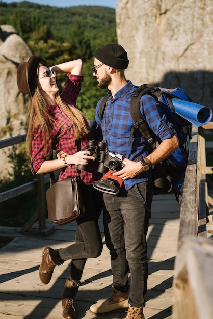 Ein Paar, das durch die Berge reist und Hipster-Kleidung mit Rucksack, Vintage-Kamera und Fernglas trägt