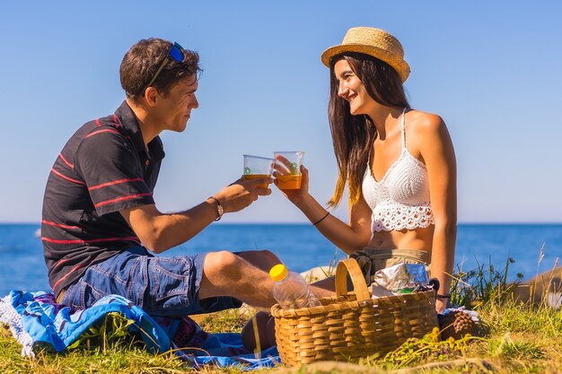 Ein Paar, das mit den wiederverwendbaren Gläsern mit Orangensaft in den Bergen am Meer röstet und die Hitze genießt