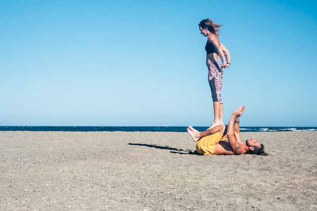 Ein paar Erwachsene, die schweigend Yoga oder Acroyoga am Strand machen - Frau und Mann konzentrieren sich auf die Zusammenarbeit - Stadt im Hintergrund