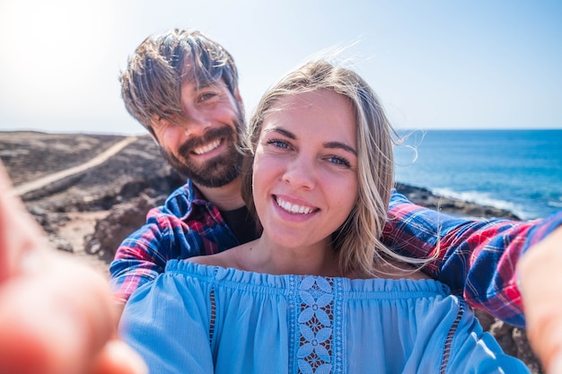 Ein Paar Erwachsene und Freunde, die zusammen mit ihren vier Händen ein Selfie machen - zwei verliebte Menschen, die das Telefon zusammen mit dem Strand im Hintergrund halten