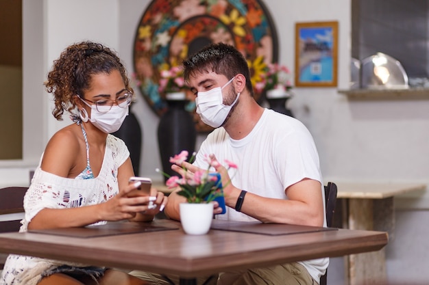 Ein paar Freunde, die Sicherheit sprechen, sitzen in einem Restaurant im Freien und tragen eine Sicherheitsmaske gegen die Covid-19-Coronavirus-Pandemie. Neues normales Lebenskonzept