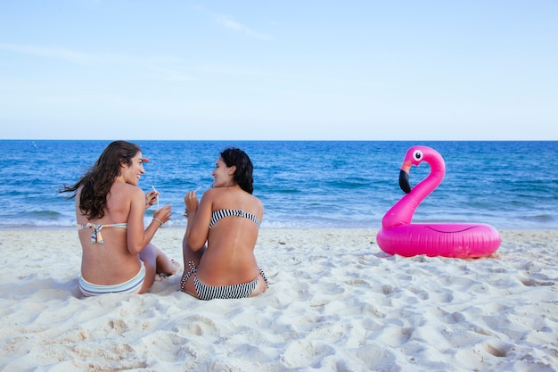 Ein paar Freundinnen, die sich verbinden und einen Drink am Strand teilen