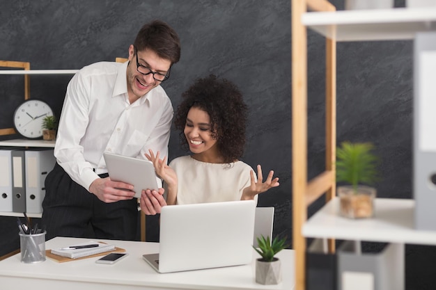 Ein paar Geschäftspartner, die im modernen Büro arbeiten. Zwei Mitarbeiter, die am Laptop arbeiten, Informationen mit digitalem Tablet vergleichen, Platz kopieren