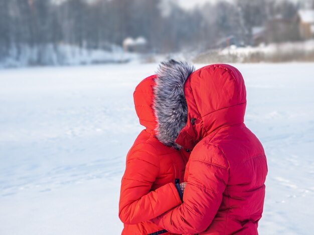 Ein Paar in roten Jacken im Winter umarmt sich in der Kälte.