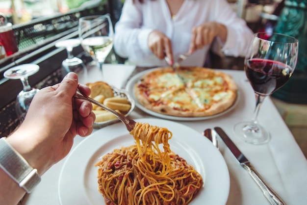 Ein Paar isst im Restaurant Pasta und Pizza und trinkt Wein aus der Ego-Perspektive ohne Gesicht