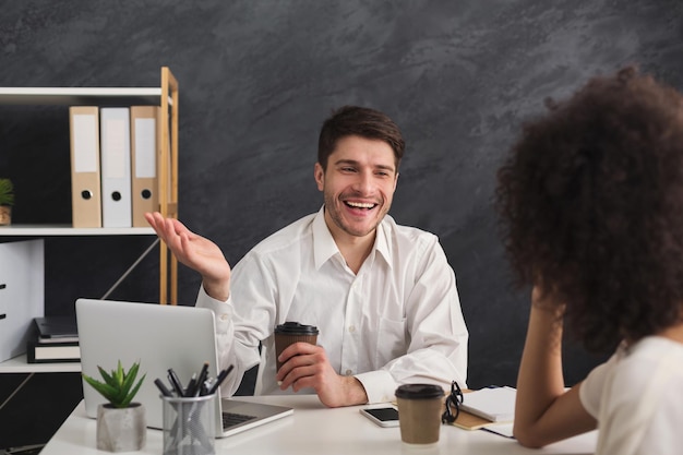 Ein paar junge Geschäftspartner, die im modernen Büro arbeiten. Lächelnder Mann, der mit seinem Kollegen ein neues Projekt bespricht, während er Kaffee trinkt, Platz kopieren