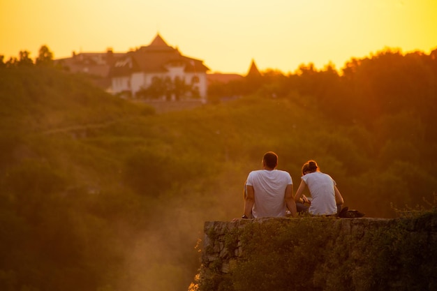 Ein paar junge Leute sitzen am Rand einer Klippe wie der Sonnenuntergang