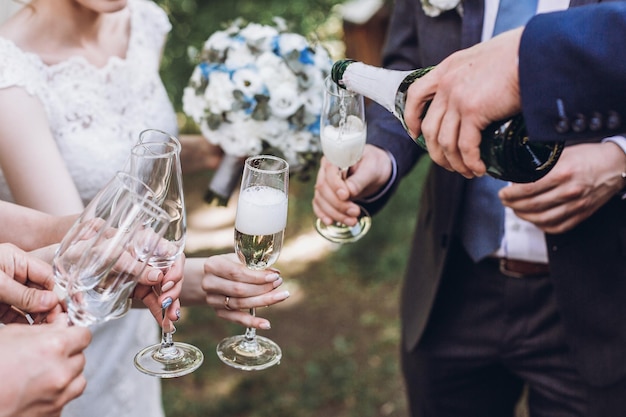 Ein paar Jungvermählten Braut und Bräutigam zusammen mit Brautjungfern und Trauzeugen trinken Champagner im Freien Hände Nahaufnahme Hochzeitsfeier mit Freunden