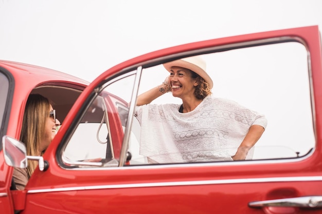 Ein paar kaukasische Frauen mittleren Alters bei Freizeitaktivitäten im Freien in der Nähe und sitzen auf einem roten Oldtimer, der bereit ist zu reisen