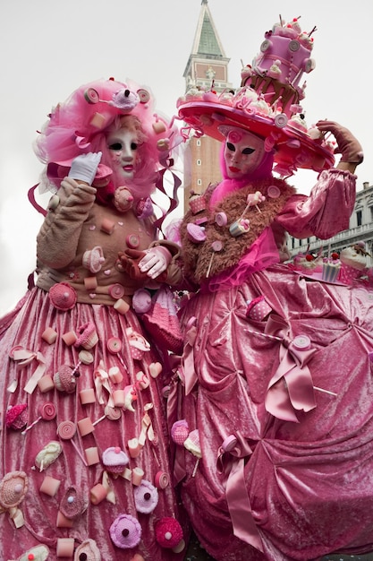 Ein paar Leute, die sich für den Karneval in Venedig verkleidet haben und rosa Süßigkeiten tragen