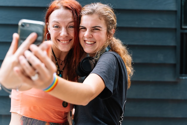 Foto ein paar mädchen mit einem lgtb-flaggenarmband machen ein selfie mit einem telefon auf der straße