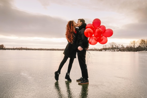 Ein Paar mit Ballons küsst sich in voller Länge, während sie gegen den Himmel stehen