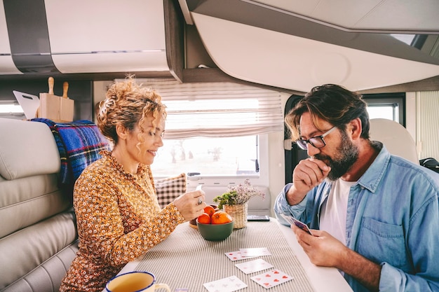 Ein Paar mittleren Alters genießt die Zeit beim gemeinsamen Kartenspielen im Reisemobil nach Hause. Menschen, die die Zeit im Urlaub genießen, lächeln und Spaß haben