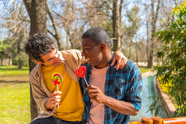 Ein paar multiethnische Männer essen ein Lollipop-LGBT-Konzept, haben Spaß und lächeln in einem Park