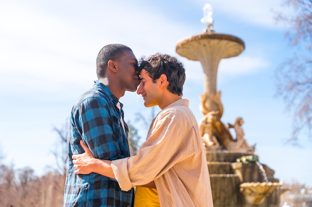 Ein paar multiethnische männer in einem lgbt-konzept eines stadtbrunnens in einer romantischen pose, die sich auf die stirn küssen