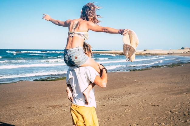 Ein paar schöne Erwachsene verloben und heiraten zusammen am Strand - Frau auf den Schultern des Mannes, der ihn anschaut und lächelt