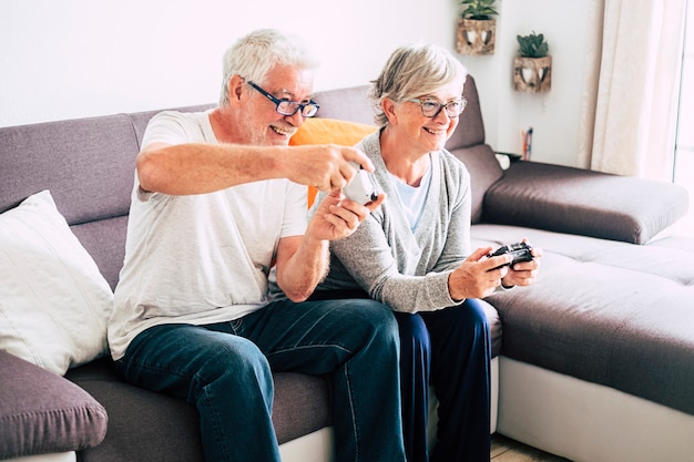 Ein paar Senioren spielen zusammen mit Videospielen und genießen es, zu Hause auf dem Sofa zu sitzen - drinnen und haben Spaß am Lebensstil