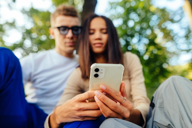 Ein Paar sitzt im Park und nutzt das Internet auf einem Smartphone, das auf den Bildschirm schaut