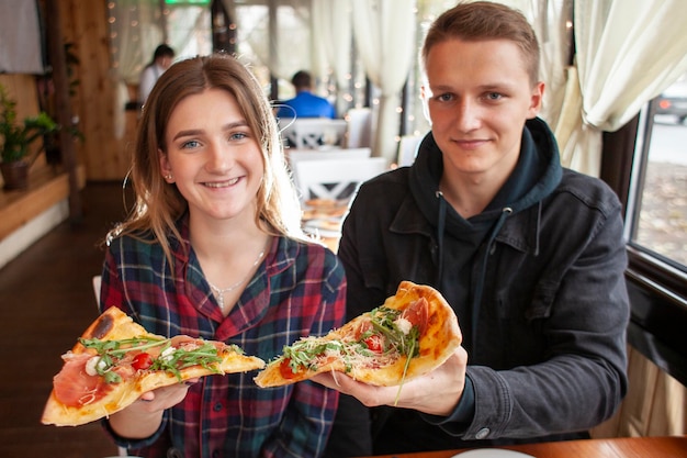 Ein Paar sitzt in einer Pizzeria und isst Pizza, ein Typ und ein Mädchen essen Fastfood-Lächeln