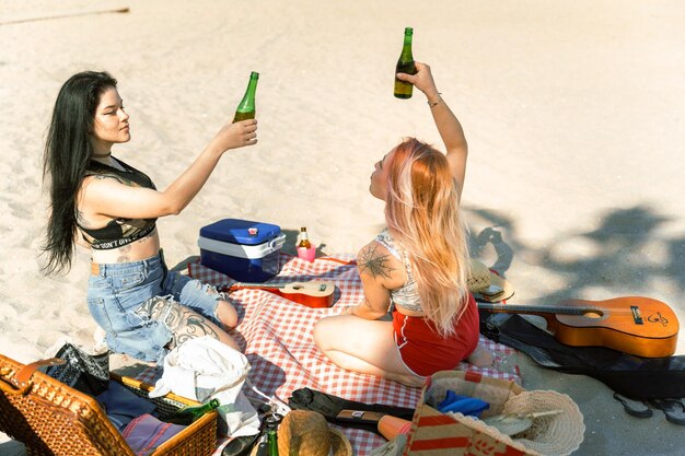 Ein Paar tätowierter und moderner Mädchen, die am Strand toasten