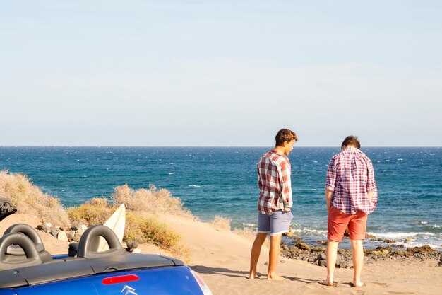 Ein paar Teenager lächeln und haben gemeinsam Spaß am Strand, Surferboy und Surf - Surfen - 20er Jahre mit Brille und Sonnenbrille im Freien warten darauf, mit Meer im Hintergrund surfen zu gehen