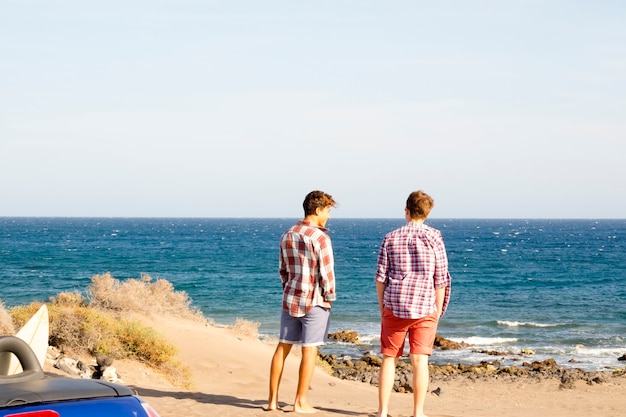 Ein paar Teenager lächeln und haben gemeinsam Spaß am Strand, Surferboy und Surf - Surfen - 20er Jahre mit Brille und Sonnenbrille im Freien warten darauf, mit Meer im Hintergrund surfen zu gehen