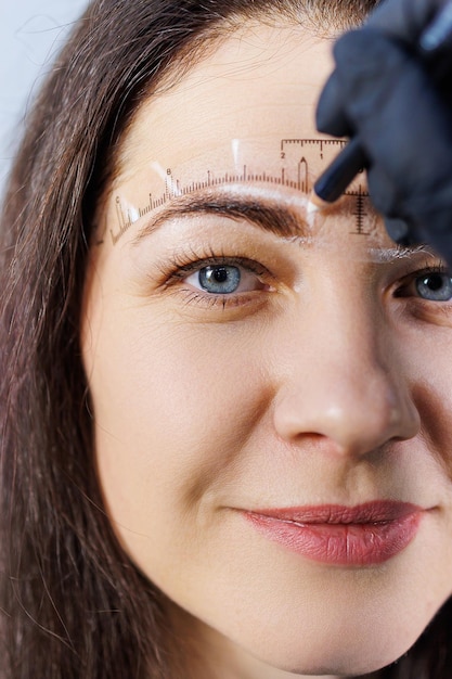 Foto ein permanent-make-up-künstler markiert die augenbrauen einer frau mit einem bleistift. kometologisches verfahren zur permanent-make-up-pflege des gesichts einer frau