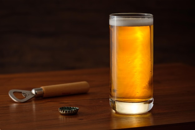 Foto ein pintglas goldenes lagerbier mit flaschenöffner und kappe auf einem holztisch