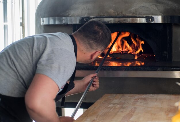 ein Pizza-Mann zieht eine Pizza aus einem neapolitanischen Ofen