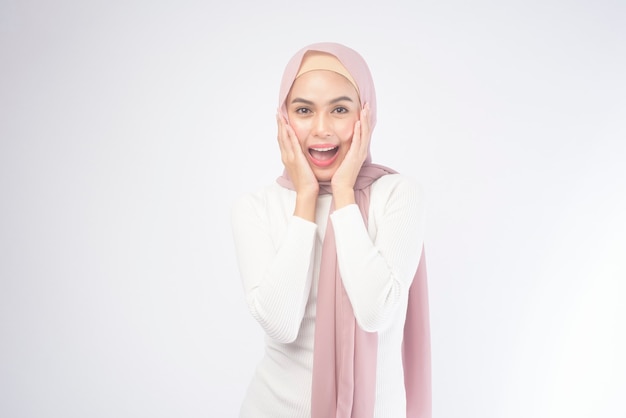 Ein Porträt der jungen lächelnden muslimischen Frau, die einen rosa Hijab auf Weiß trägt.