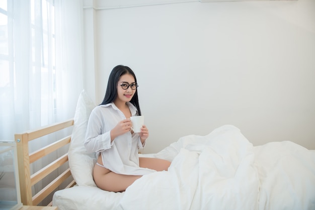 Ein Porträt der schönen asiatischen Frau, die Kaffee auf dem Bett trinkt