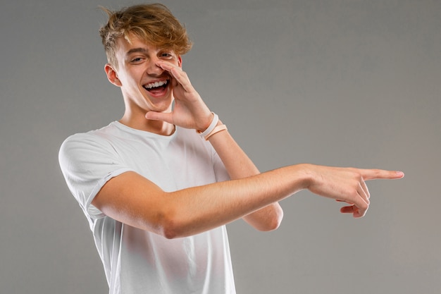 Ein Porträt des jungen kaukasischen Mannes mit dem kurzen roten lockigen Haar im weißen T-Shirt, das über etwas lokalisiert auf einem grauen Hintergrund lacht