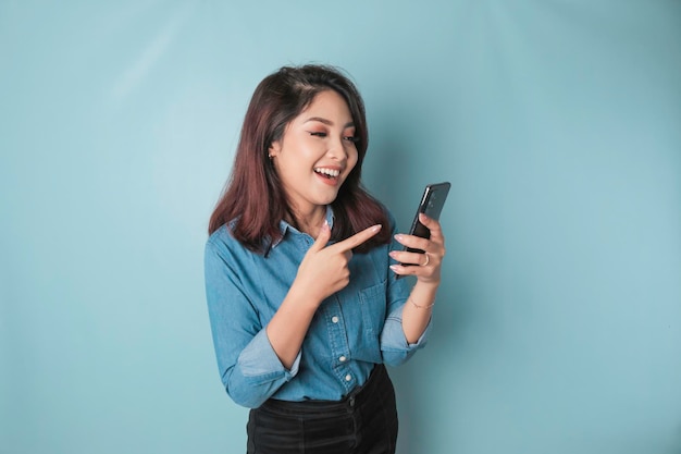 Ein Porträt einer glücklichen asiatischen Frau lächelt und hält ihr Smartphone in einem blauen Hemd, das durch einen blauen Hintergrund isoliert ist