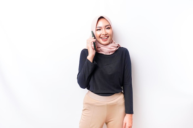 Ein Porträt einer glücklichen asiatischen muslimischen Frau, die einen Hijab trägt und ihr Telefon isoliert durch weißen Hintergrund hält