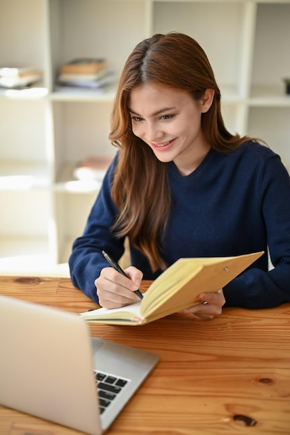 Ein Porträt einer schönen asiatischen Studentin, die sich Notizen zu ihrem Buch macht