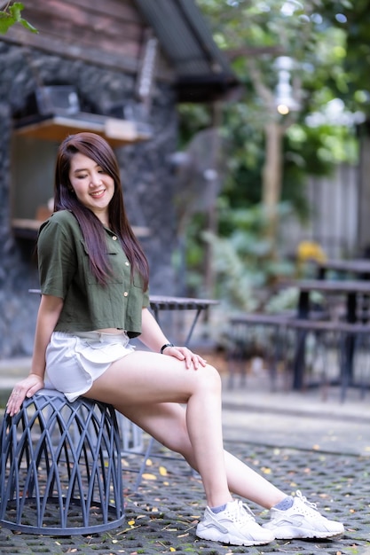 Ein Porträt einer schönen, glücklichen asiatischen Reisenden mit bräunlich-grünem Kleid, stilvollem Hipster Sommer sonniger Lebensstil auf der Straße im Freien an einem sonnigen Sommertag im Parkhintergrund