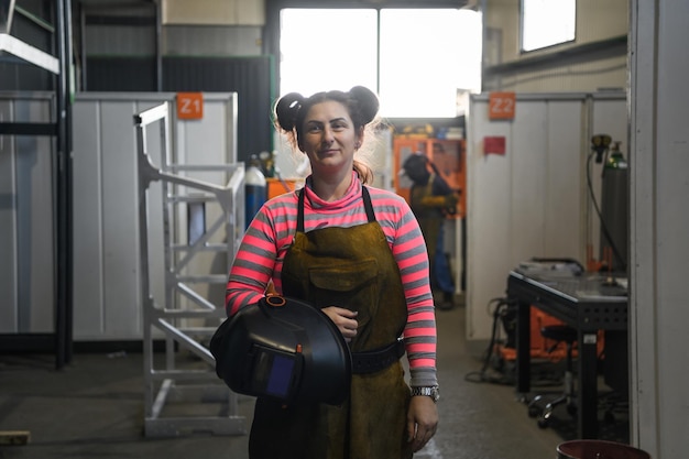 Ein Porträt einer Schweißerin, die einen Helm in der Hand hält und sich auf einen Arbeitstag in der Metallindustrie vorbereitet. Hochwertiges Foto