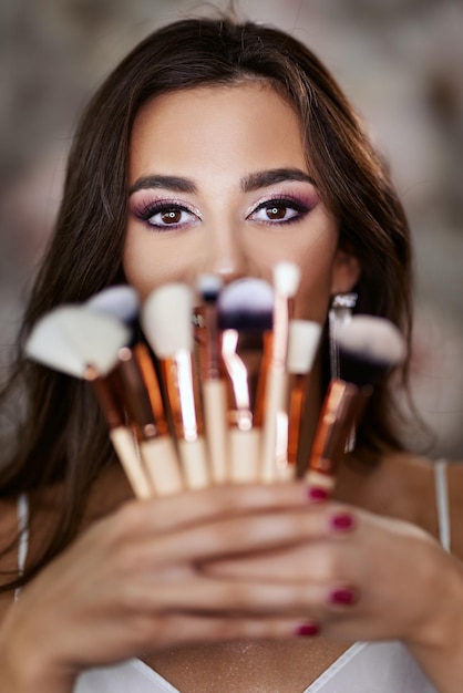 Foto ein porträt einer süßen jungen frau mit schönen augen, die make-up-pinsel hält und ein schönes make-up auf ihrem gesicht darstellt.