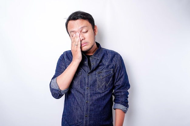 Ein Porträt eines asiatischen Mannes, der ein blaues Hemd trägt, das von weißem Hintergrund isoliert ist, sieht deprimiert aus