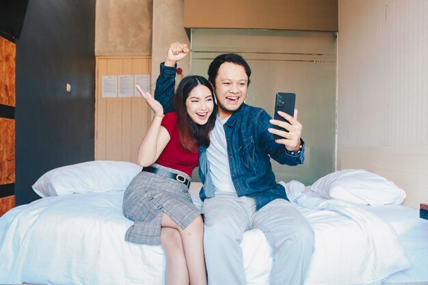 Ein Porträt eines glücklichen asiatischen Paares, das auf sein Smartphone lächelt