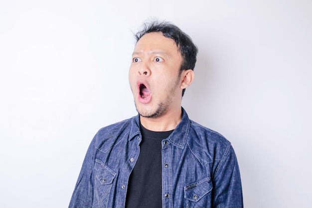 Ein Porträt eines schockierten asiatischen Mannes, der ein marineblaues Hemd trägt, das durch einen weißen Hintergrund isoliert ist