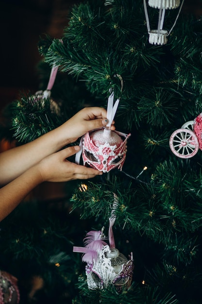 Ein Porträt eines schwarzen Mädchens in einem roten Kleid schmückt einen Weihnachtsbaum mit einer roten Glaskugel zu Hause