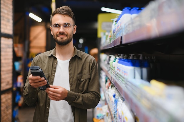 Ein positiver männlicher Kunde wählt ein neues Shampoo in der Haarsektion des Supermarkts aus