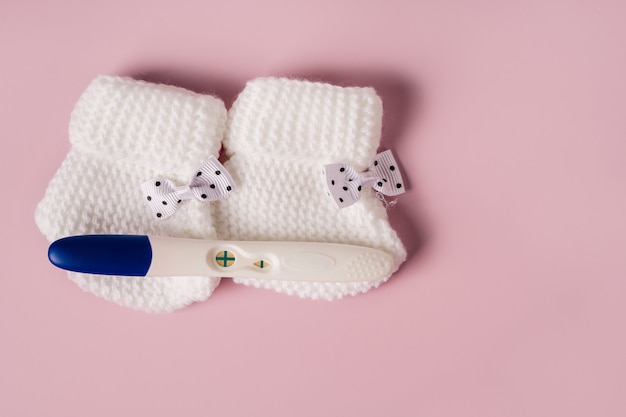 Foto ein positiver schwangerschaftstest und babyschuhe auf rosa hintergrund warten auf das baby
