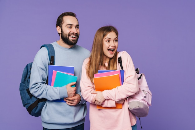 ein positives glückliches Liebespaar Freunde Studenten isoliert über lila Wand mit Büchern.