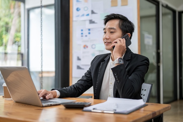 Ein professioneller asiatischer Geschäftsmann ruft seinen Kunden an, während er an seinem Schreibtisch im Büro arbeitet