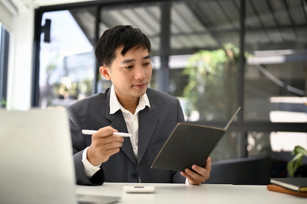 Ein professioneller asiatischer Geschäftsmann überprüft seinen Besprechungsplan in seinem Planerbuch