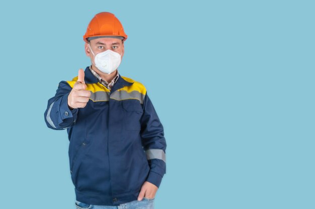 Ein professioneller Baumeister in einem orangefarbenen Bauarbeiterhelm und einer Schutzmaske streckte seine Hand mit dem Zeigefinger nach vorne aus, blauer Hintergrund